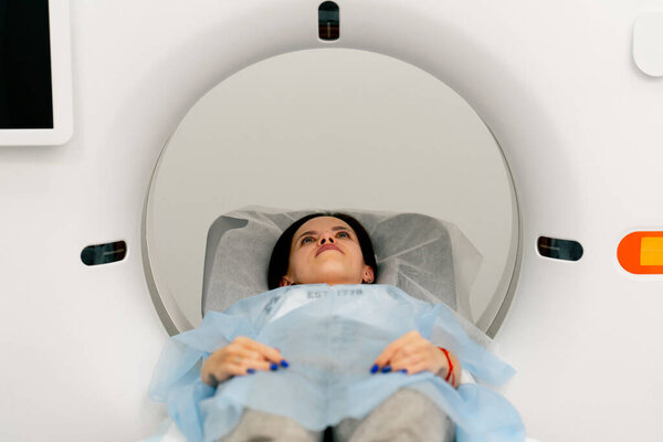 Девушка в медицинском халате лежит на подвижном диване магнитно-резонансной томографии и готовится к диагностике