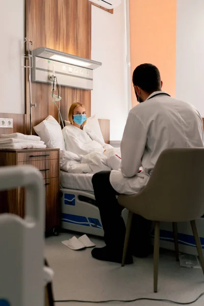 A girl in a hospital room in a medical mask in quarantine describes to a doctor complaints about her health
