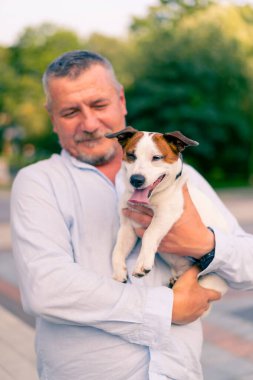 Yetişkin sakallı bir adamın portresi. Küçük köpeğini tutuyor. Jack Russell Terrier cinsi.
