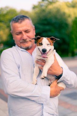 Yetişkin sakallı bir adamın portresi. Küçük köpeğini tutuyor. Jack Russell Terrier cinsi.