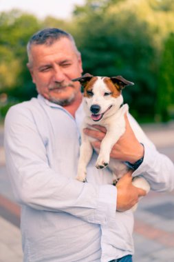 Yetişkin sakallı bir adamın portresi. Küçük köpeğini tutuyor. Jack Russell Terrier cinsi.