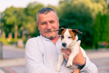 Yetişkin sakallı bir adamın portresi. Küçük köpeğini tutuyor. Jack Russell Terrier cinsi.