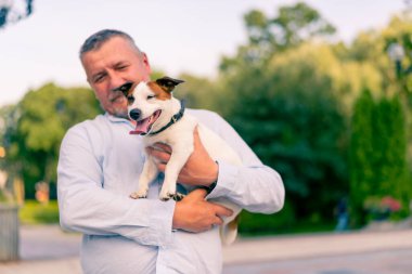 Yetişkin sakallı bir adamın portresi. Küçük köpeğini tutuyor. Jack Russell Terrier cinsi.