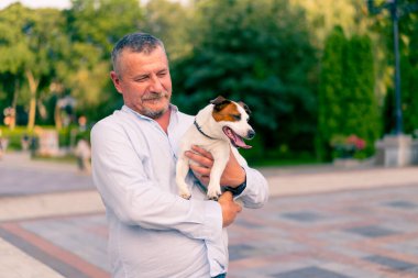 Yetişkin sakallı bir adamın portresi. Küçük köpeğini tutuyor. Jack Russell Terrier cinsi.