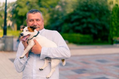 Yetişkin sakallı bir adamın portresi. Küçük köpeğini tutuyor. Jack Russell Terrier cinsi.