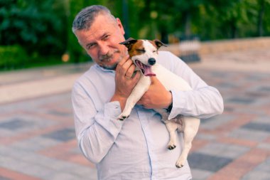 Yetişkin sakallı bir adamın portresi. Küçük köpeğini tutuyor. Jack Russell Terrier cinsi.