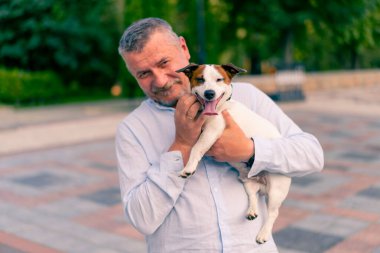 Yetişkin sakallı bir adamın portresi. Küçük köpeğini tutuyor. Jack Russell Terrier cinsi.
