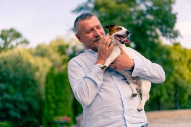 Yetişkin sakallı bir adamın portresi. Küçük köpeğini tutuyor. Jack Russell Terrier cinsi.