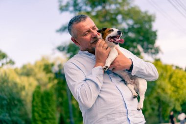Yetişkin sakallı bir adamın portresi. Küçük köpeğini tutuyor. Jack Russell Terrier cinsi.