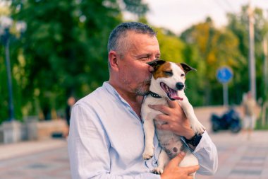 Yetişkin sakallı bir adamın portresi. Küçük köpeğini tutuyor. Jack Russell Terrier cinsi.