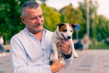 Yetişkin sakallı bir adamın portresi. Küçük köpeğini tutuyor. Jack Russell Terrier cinsi.
