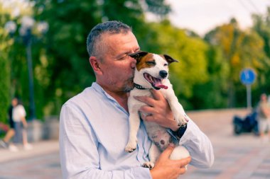 Yetişkin sakallı bir adamın portresi. Küçük köpeğini tutuyor. Jack Russell Terrier cinsi.