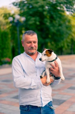 Yetişkin sakallı bir adamın portresi. Küçük köpeğini tutuyor. Jack Russell Terrier cinsi.