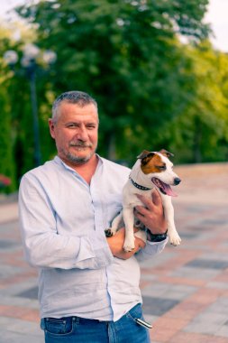 Yetişkin sakallı bir adamın portresi. Küçük köpeğini tutuyor. Jack Russell Terrier cinsi.