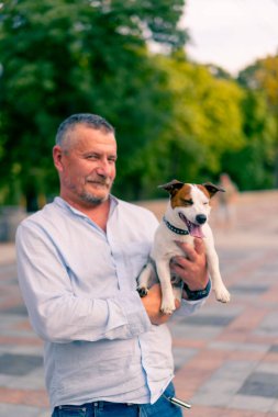 Yetişkin sakallı bir adamın portresi. Küçük köpeğini tutuyor. Jack Russell Terrier cinsi.