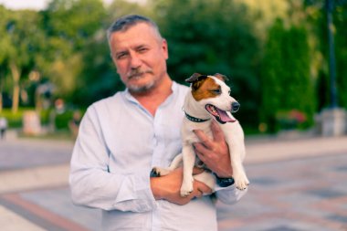 Yetişkin sakallı bir adamın portresi. Küçük köpeğini tutuyor. Jack Russell Terrier cinsi.