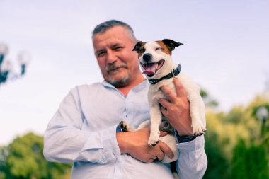 Yetişkin sakallı bir adamın portresi. Küçük köpeğini tutuyor. Jack Russell Terrier cinsi.
