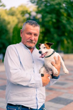 Yetişkin sakallı bir adamın portresi. Küçük köpeğini tutuyor. Jack Russell Terrier cinsi.