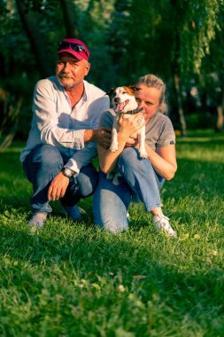 Mutlu bir ailenin portresi. Yetişkin bir adam ve bir kadın Jack Russell teriyerinden bir köpekle yürüyüşe çıkmış. Parkta hayvanlara sarılıyorlar.