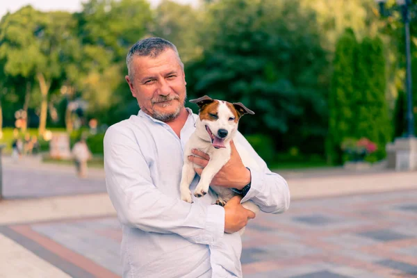 Yetişkin sakallı bir adamın portresi. Küçük köpeğini tutuyor. Jack Russell Terrier cinsi.