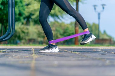 Spor sahasındaki kasları güçlendirmek için elastik bir bantla egzersiz yapan kız spor eğitmeninin bacakları.