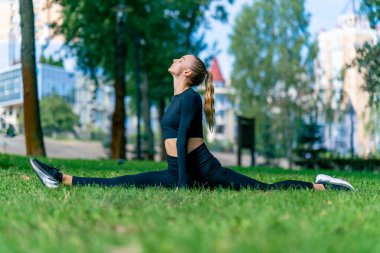 Genç ve güzel bir kız, sabah antrenmandan sonra parkta oturup esneme hareketleri yapıyor.