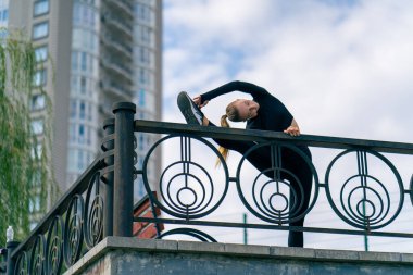 Sabah antrenmanı sırasında bir jimnastikçi bacağını metal bir tarafa atarak esnetir.