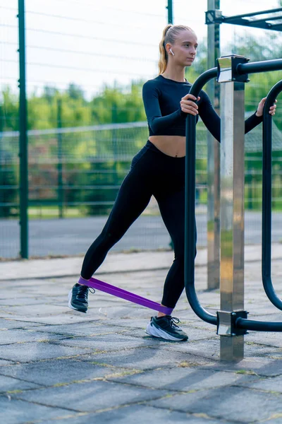 Focused girl athlete performs exercises with a sports elastic band on street exercise machines