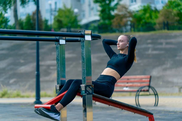 Atletik genç bir kadın sabah sporu yaparken sokaktaki bir spor makinesinde karın kaslarını şişiriyor.