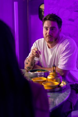 Restoranda yemek çubuklarıyla geleneksel Kore mutfağından hoşlanan ve randevuda bir kızla tartışan bir adamın portresi.