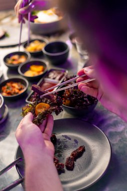 Masanın üzerinde ızgarası ve kapüşonu olan bir Kore restoranında aşık bir çift yemek çubuğu konsepti olan çeşitli geleneksel yemekleri tadıyor.