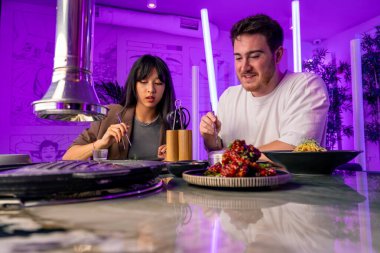 Masanın üzerinde ızgarası ve kapüşonu olan bir Kore restoranında aşık bir çift yemek çubuğu konsepti olan çeşitli geleneksel yemekleri tadıyor.