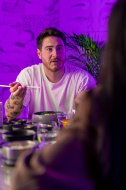 Restoranda yemek çubuklarıyla geleneksel Kore mutfağından hoşlanan ve randevuda bir kızla tartışan bir adamın portresi.