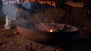 Bir kadının eli, bir kamp alanındaki vahşi bir ateşte, ızgarada et pişiriyor.