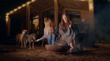 Kız arkadaşlar geceleri şöminenin başında köpekleri ile oturuyor ellerini ısıtıyor ve ahşap evlerinin yanında konuşuyorlar.
