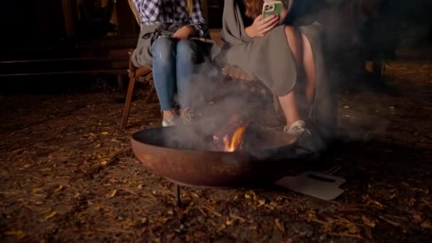 夜中に外で一緒に座っているガールフレンドのショット 火が彼らの手を暖め 木製の家の外でチャット — ストック動画