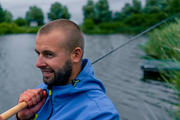 釣りロッドスピニングと川岸スポーツフィッシングに座っているプロのツールを持つポートレートフィッシャーマン — ストック写真