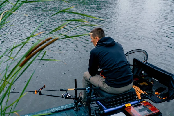 釣りロッドまたはスピニングと川岸の背面ビューに座っているプロのツールを持つ漁師 湖のスポーツ釣りから魚を引っ張る — ストック写真
