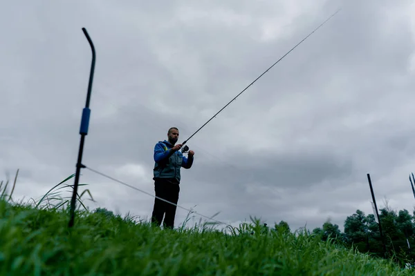 釣り棒または回転棒および湖のスポーツの釣りから川岸に立っている専門用具が付いている漁師 — ストック写真