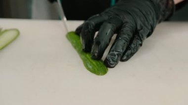 Profesyonel mutfakta suşi yaparken profesyonel bir mutfak bıçağıyla salatalığı kesen eldivenli bir suşi makinesinin yakın çekimi.