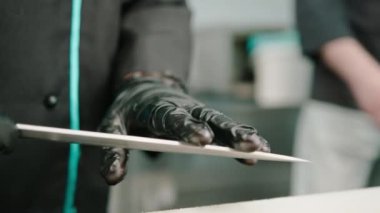 Suşi hazırlamaya başlamadan önce parmaklarını bir şefin bıçağının ucunda gezdiren siyah eldivenli bir elin yakın çekimi.
