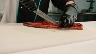 Eldivenli bir suşi şefinin mutfak masasında suşi yaparken profesyonel bir bıçakla yılan balığı filetosu keserken yakın çekimi.