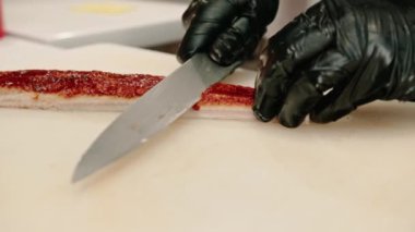 Eldivenli bir suşi şefinin mutfak masasında suşi yaparken profesyonel bir bıçakla yılan balığı filetosu keserken yakın çekimi.