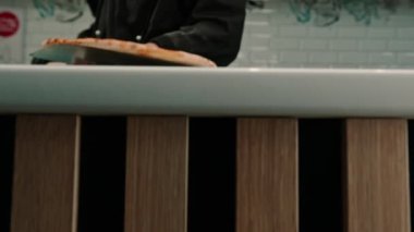 Yakın plan. Bir pizzacı fırından pizza kürekleriyle pizza alır ve pizzacıdaki pizza kutusuna koyar.