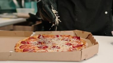 Yakın plan bir pizza şefi pizzanın mutfağındaki teslimat kutusunda duran pizzanın üzerine mozzarella peyniri serpiyor.