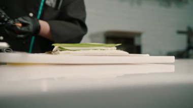 Siyah eldivenli bir suşi makinesinin yakın plan çekimi. Suşi hazırlamak için pilav nori çarşafları somon peyniri, salatalık peyniri, avokado, mutfak masası.