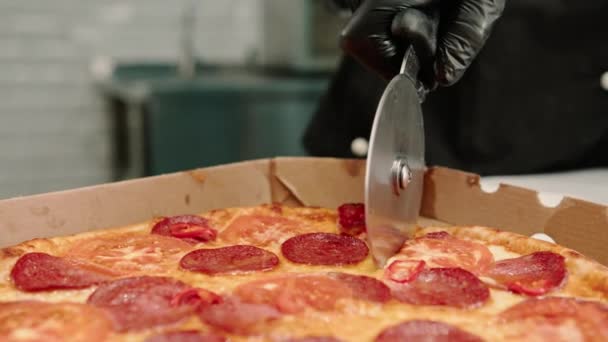 特写披萨厨师在披萨店的厨房里用比萨饼刀把比萨饼切到了一个送货箱里 — 图库视频影像