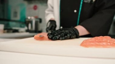 Suşi restoranının mutfağında suşi hazırlarken somon filetosunu bıçakla kesen bir aşçının yakın çekimi.