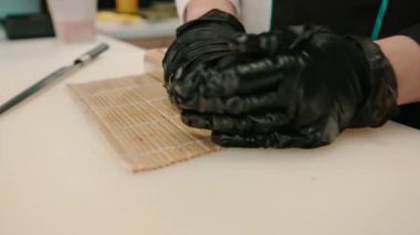 Profesyonel mutfakta somon balığı rulosu bambu suşi hasırı saran siyah eldivenli suşi makinesini kapat.