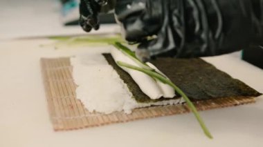 Siyah eldivenli bir suşi şefinin yakın plan çekimi. Suşi hazırlamak için pirinçli nori çarşaflı karides filetosu karides peynirli salatalık peynirli avokado.